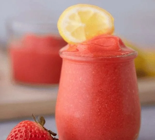 Chilled frozen strawberry lemonade in a glass with fresh strawberries and lemon slices