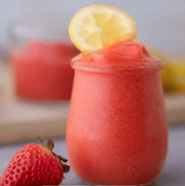 Refreshing frozen strawberry lemonade in a glass with fresh strawberries and lemon slices.