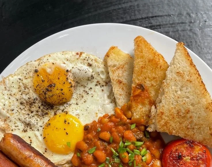 A perfectly arranged full English breakfast with eggs, bacon, sausages, and toast.
