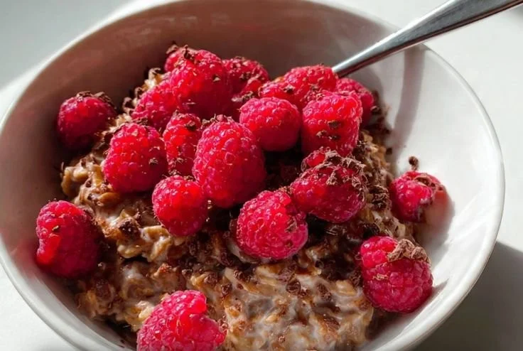 Bowl of raspberry cocoa oatmeal topped with fresh raspberries and cocoa nibs