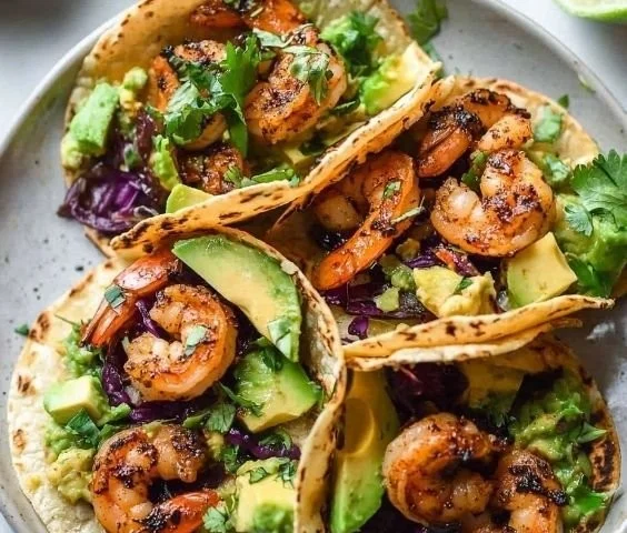 Delicious shrimp tacos topped with fresh avocado and served with lime wedges.