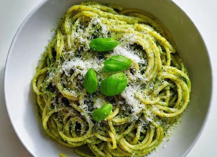 A delicious bowl of spaghetti pesto topped with fresh basil and Parmesan cheese.