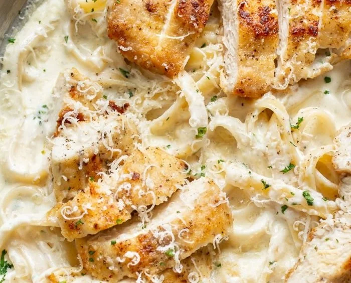 Bowl of creamy Chicken Fettuccine Alfredo topped with parsley and grated parmesan.