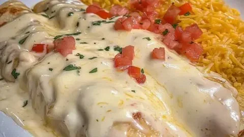 Plate of creamy queso chicken enchiladas topped with fresh herbs