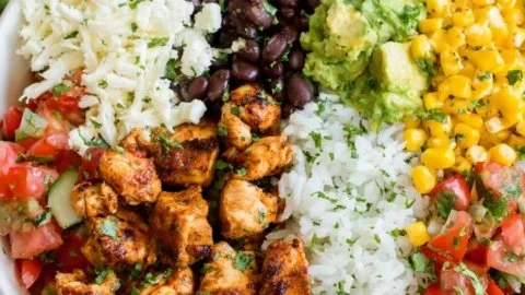 A colorful Chicken Burrito Bowl with rice, beans, chicken, and fresh toppings.
