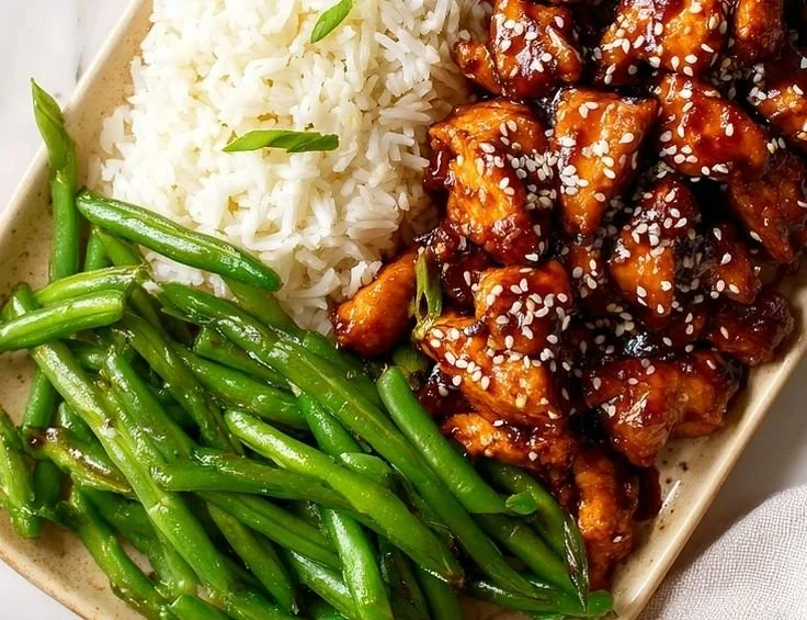 Plate of easy high protein sesame chicken garnished with sesame seeds and green onions.