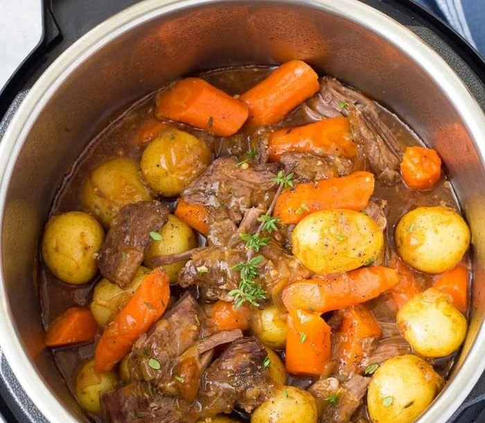 Delicious Instant Pot pot roast with vegetables and herbs served on a plate.