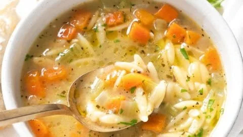 A bowl of comforting orzo soup with vegetables and herbs