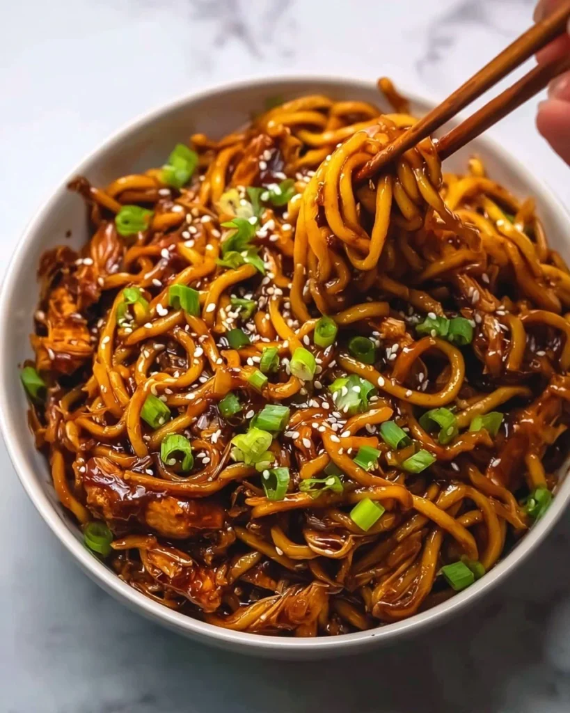 Delicious sticky garlic chicken noodles served in a bowl, garnished with herbs.